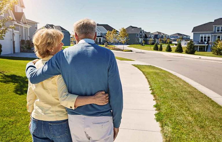 An elderly couple walking down a sidewalk hugging each other.