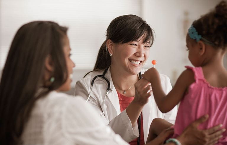 Pediatric doctor meeting with a family and smiling while working with a child.