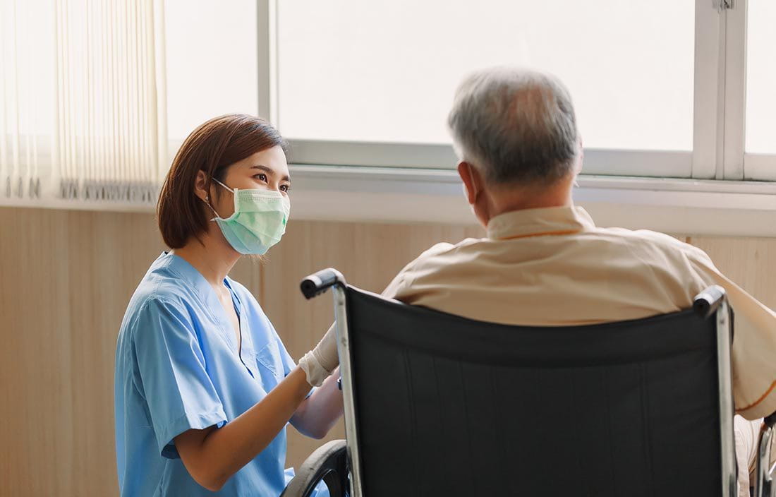 Healthcare professional kneeling down taking care of elderly patient in a chair.