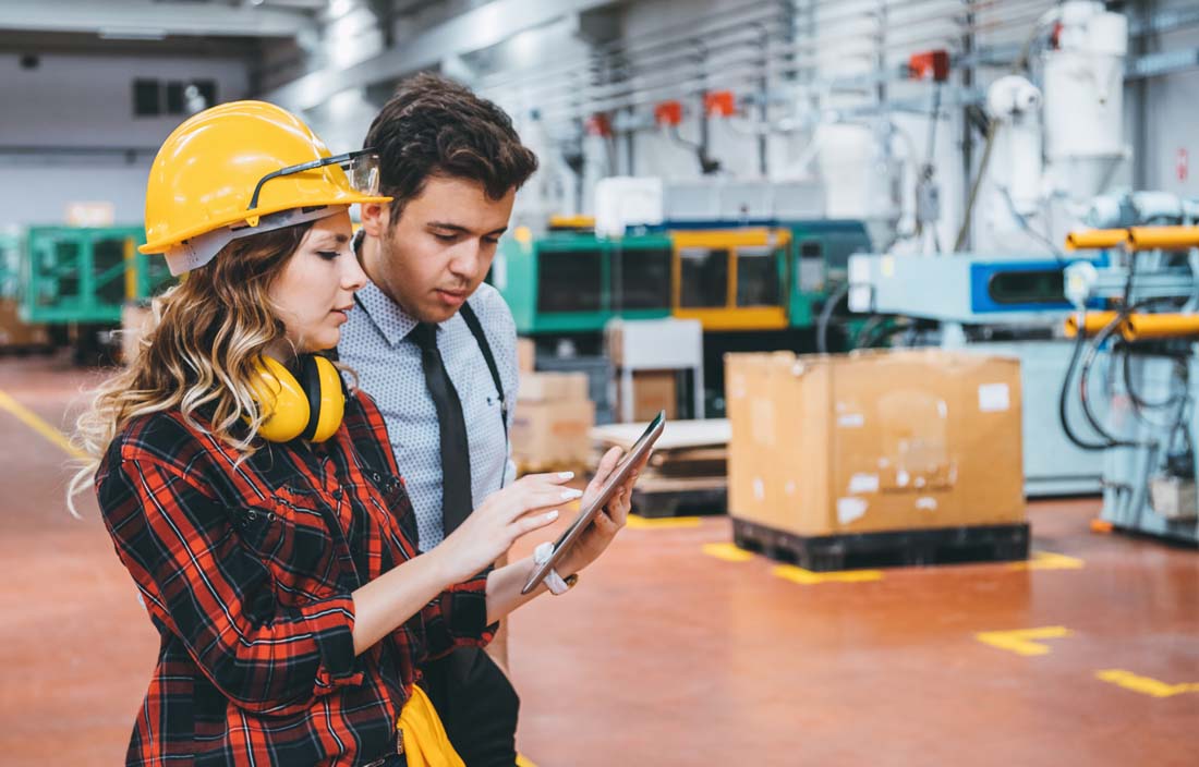 Factory worker & businessperson going over inventory in manufacturing facility.