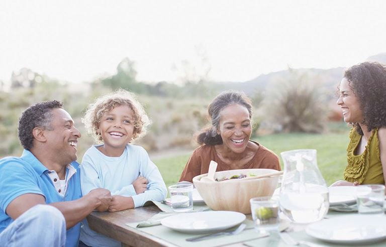 Multiple generations of a family laughing and eating dinner together.