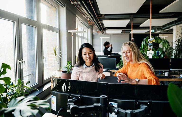 Two business professionals in front of computer monitors talking about generative AI