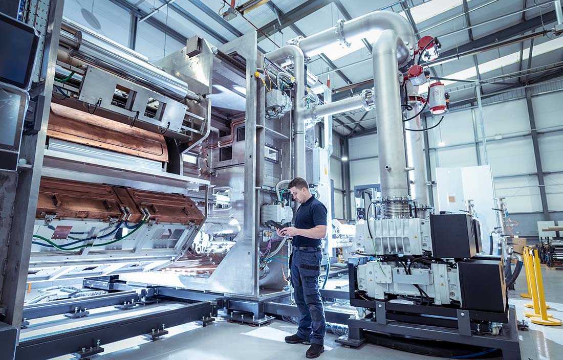 Factory worker standing next to heavy machinery while using a tablet device