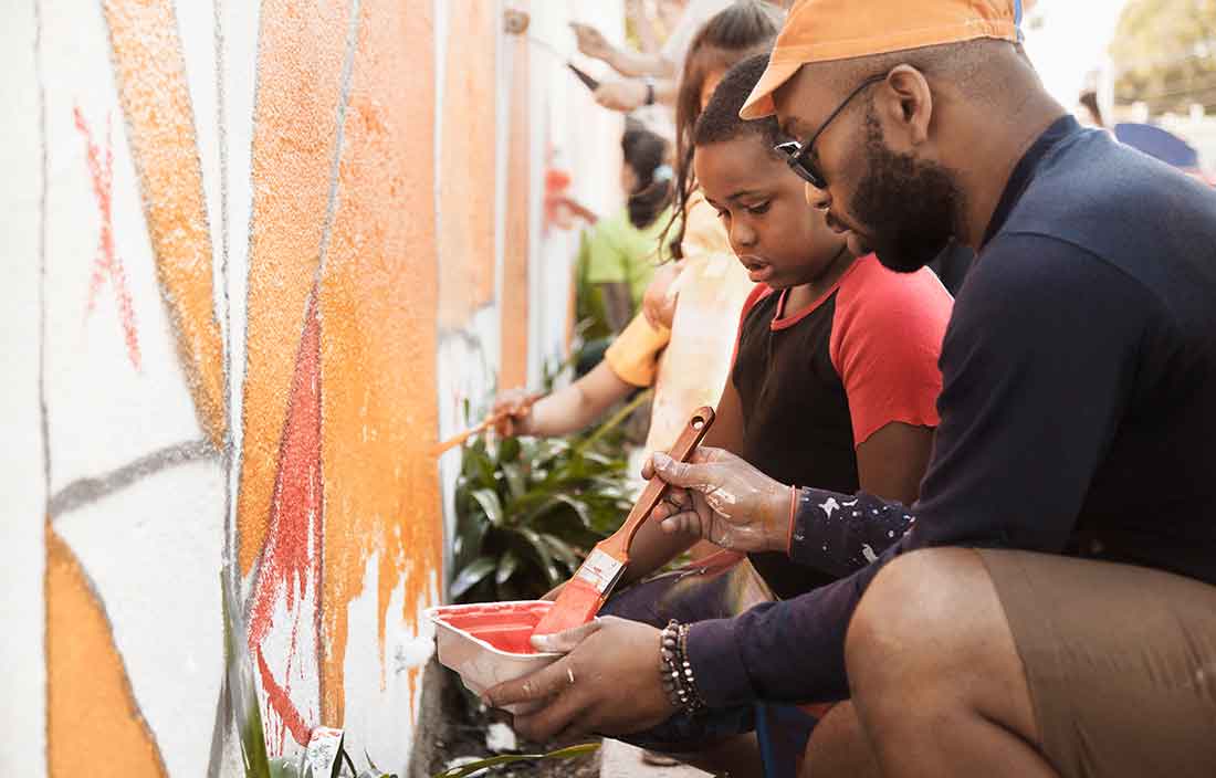 Child and adult painting a mural on a wall.