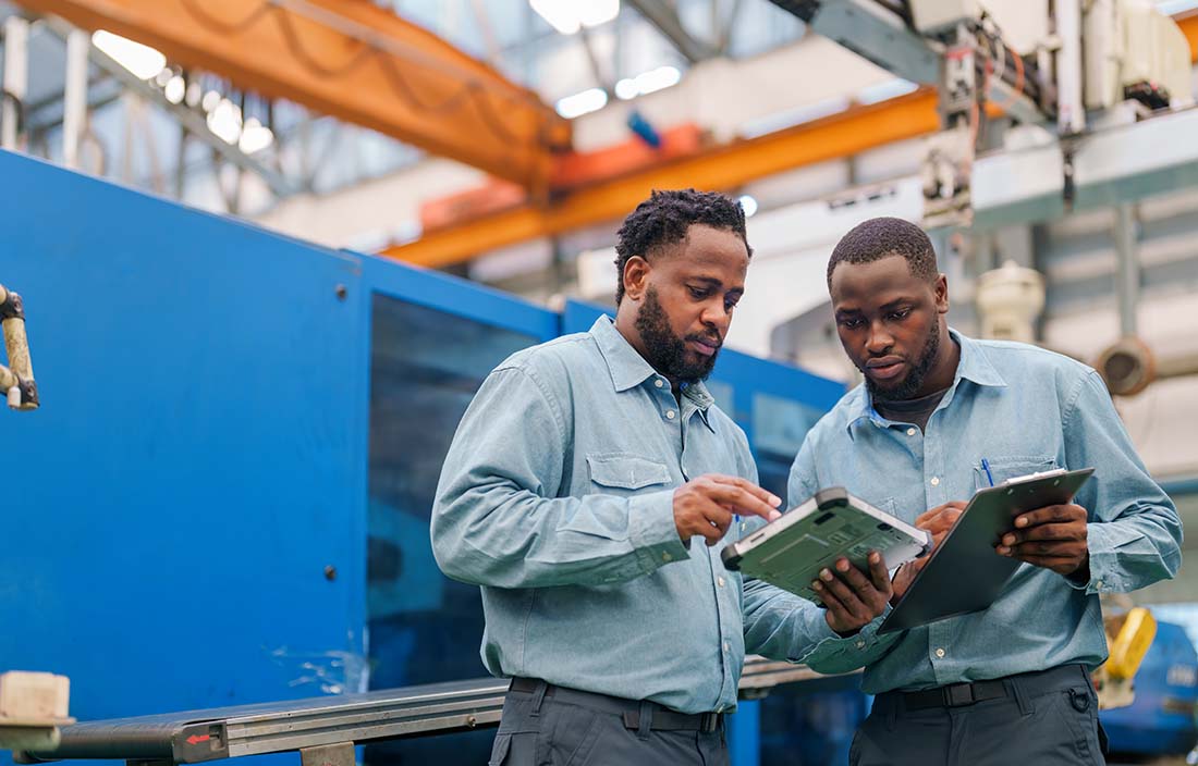 Two automotive manufacturers in a manufacturing facility looking at their tablet computers.