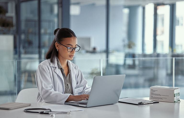 Young doctor in a medical facility typing on their laptop.