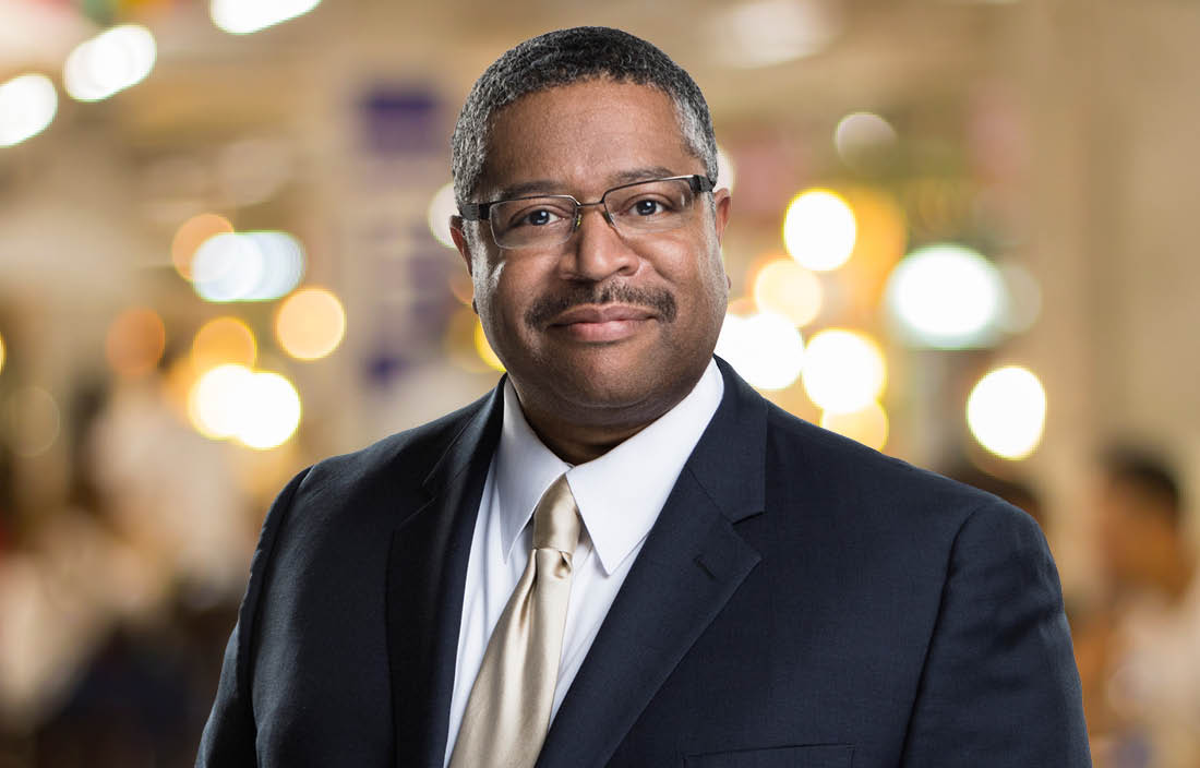 Professional photo of Paul Bryant in front of a brightly lit blurred background.