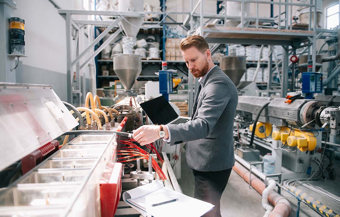 Business professional checking factory floor equipment while holding a laptop computer