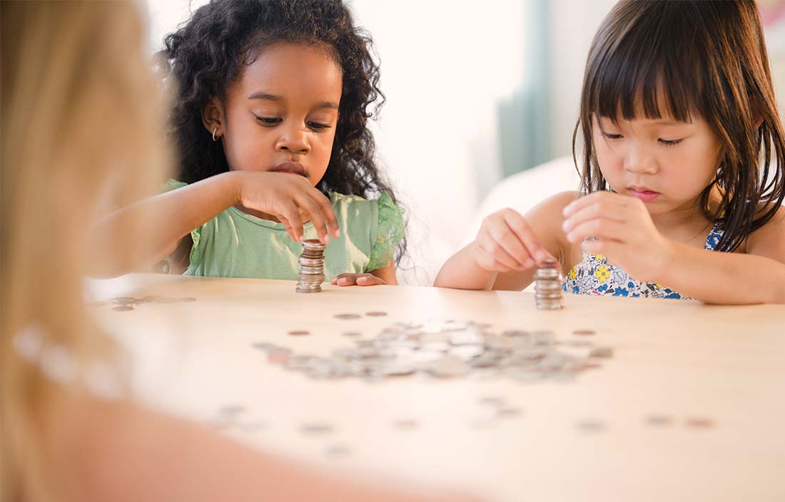 2 little girls counting money on a table in schools