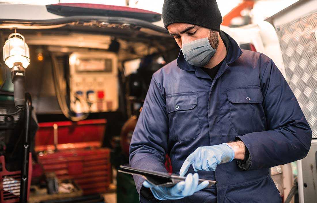 Senior living maintenance man reviewing jobs on a tablet in front of the back of his work van filled with tools.