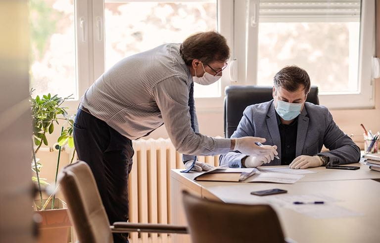 Real estate asset manager working with investor/owner to improve cash flow and NOI at a table wearing masks.