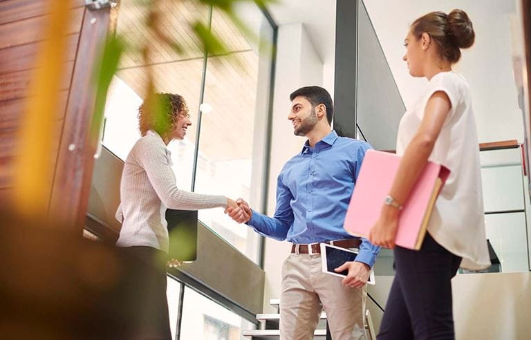 Three people greeting one another with man and woman shaking hands.