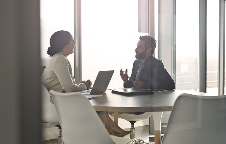 A man and woman are talking while seated at a table.