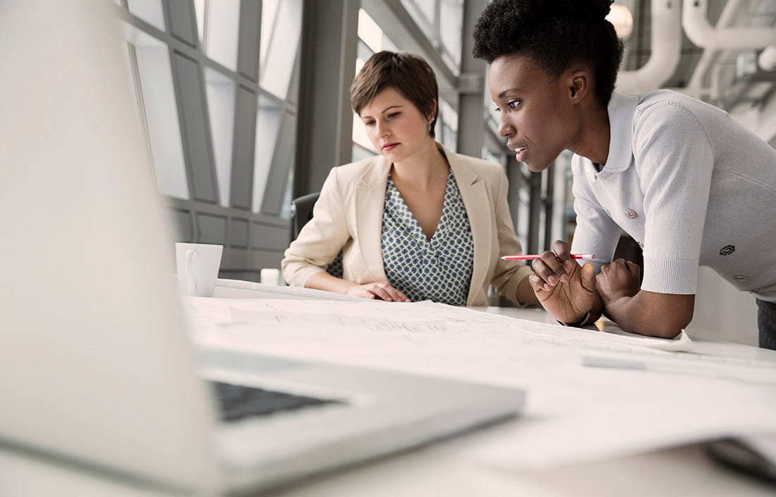 Image of two business women reviewing documents, with an open laptop in the foreground.