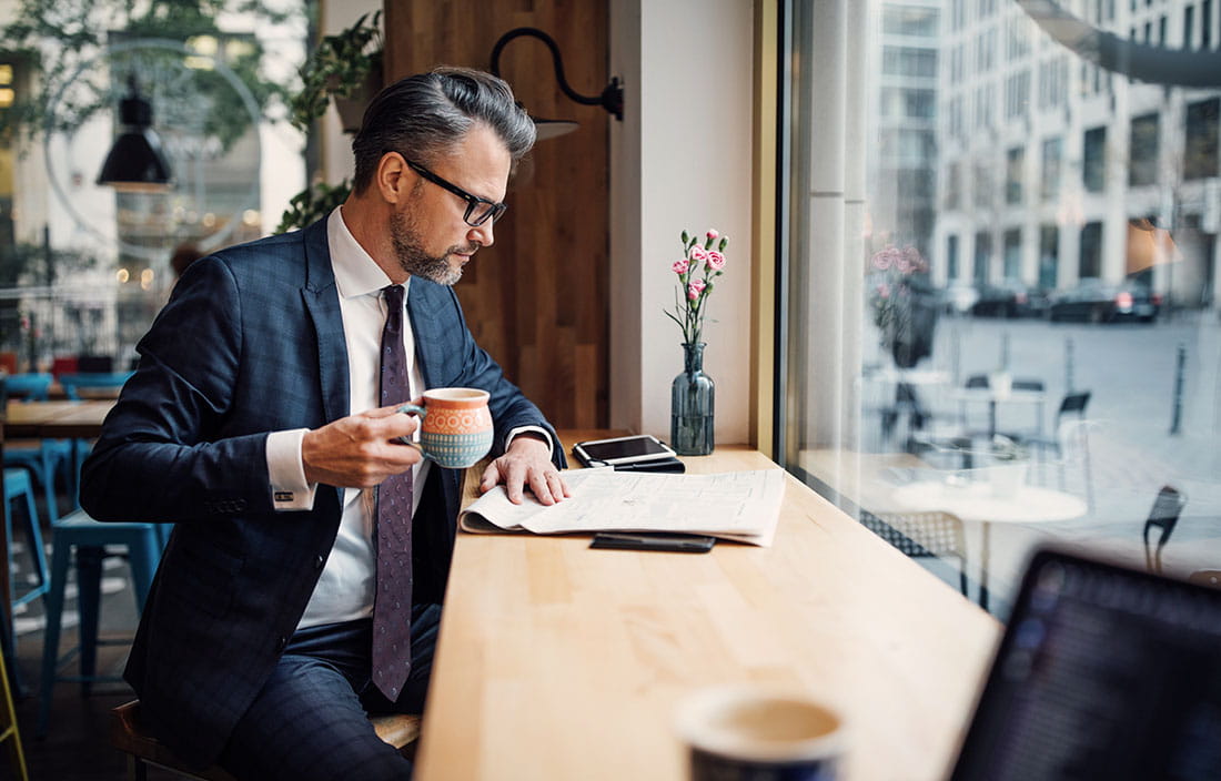 Businessman sitting at a coffee shop counter reading about the CARES Act in a newspaper.