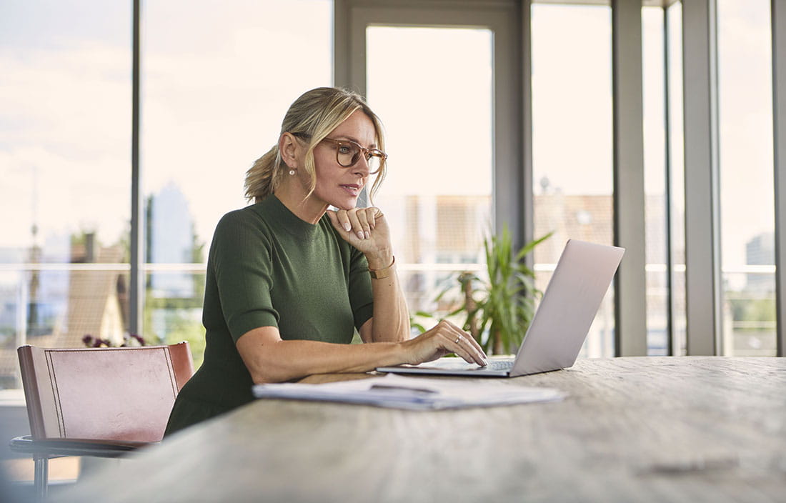 Middle aged woman sitting at a table using her laptop computer.