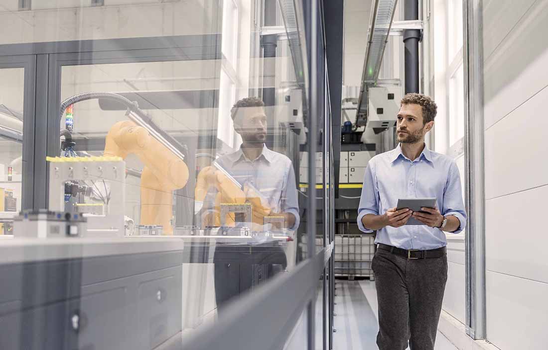 Businessman walking the manufacturing floor next to robotic equipment.