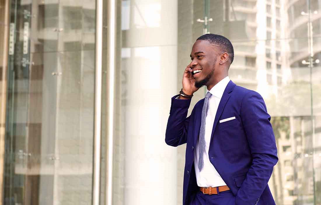 Businessperson standing outside taking a phone call wearing a blue suit.