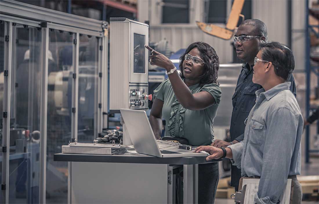 Three workers on a manufacturing floor investigating a machine.