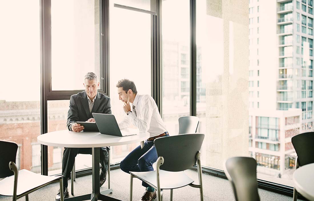 Image of two businessmen sitting at a table reviewing information on a laptop.